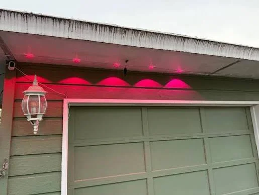 Surface-mounted retail permanent-lighting pucks and visible wiring beneath a garage soffit
